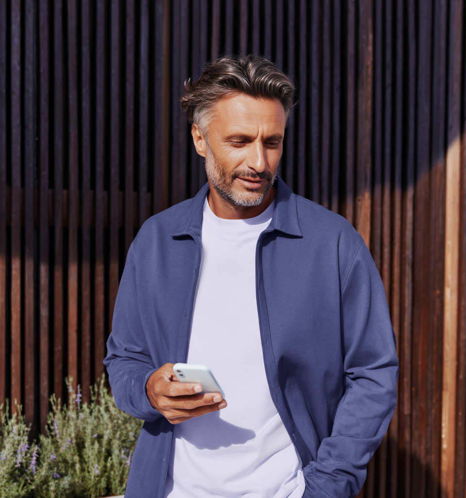 Man in a blue jacket and white shirt using a phone outdoors.